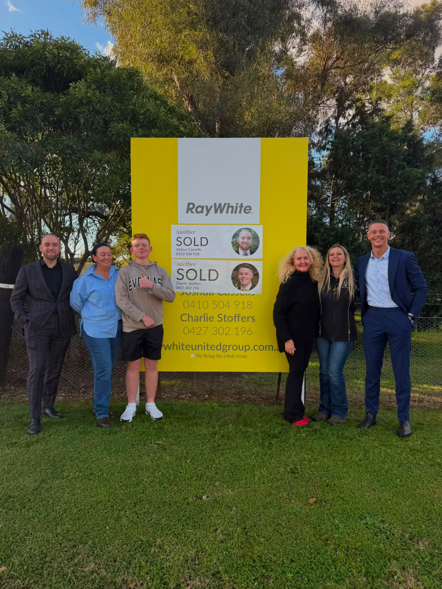 A group of sellers beside a Sold sign at their home