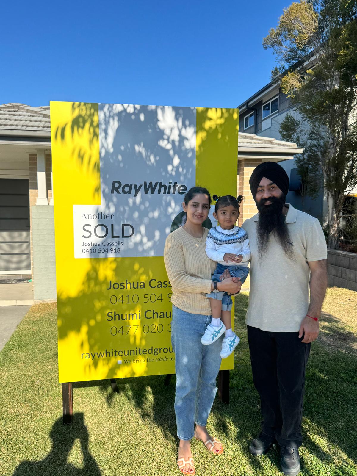 A family beside a Sold sign at their home