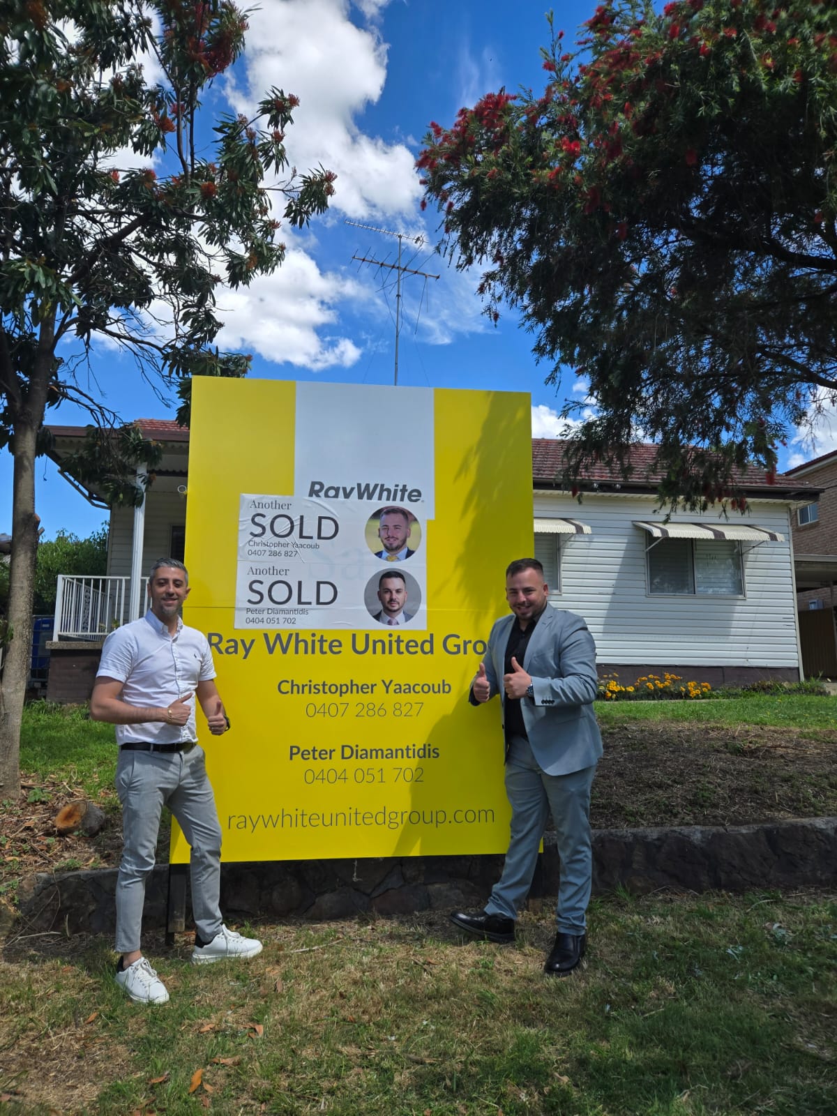 Two sellers giving a thumbs up beside a Sold sign at their home
